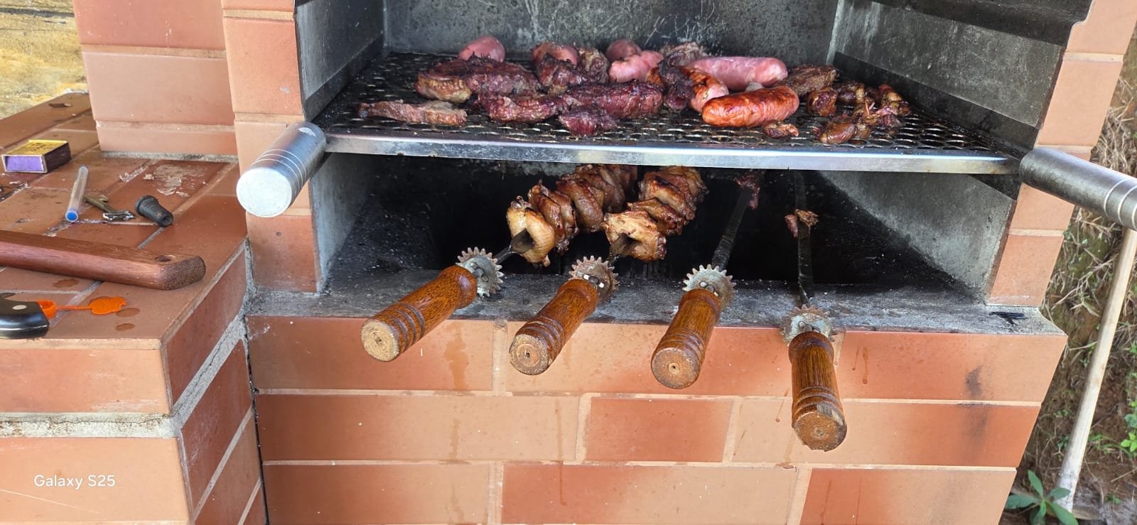 Churrasqueira de alvenaria com grelha cheia e espetos girando
