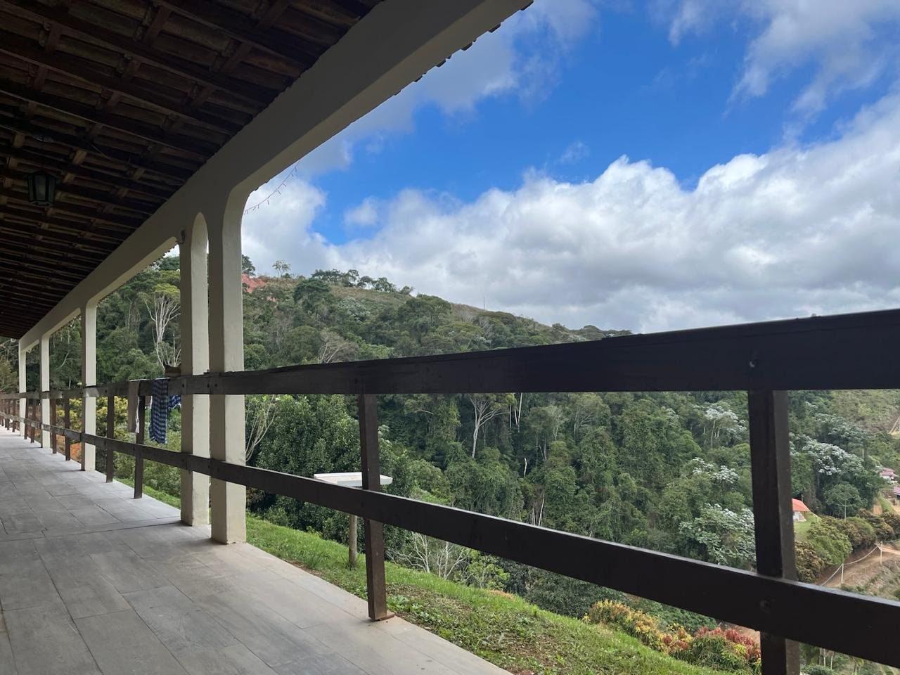 Varanda coberta com guarda-corpo de madeira e vista para a mata